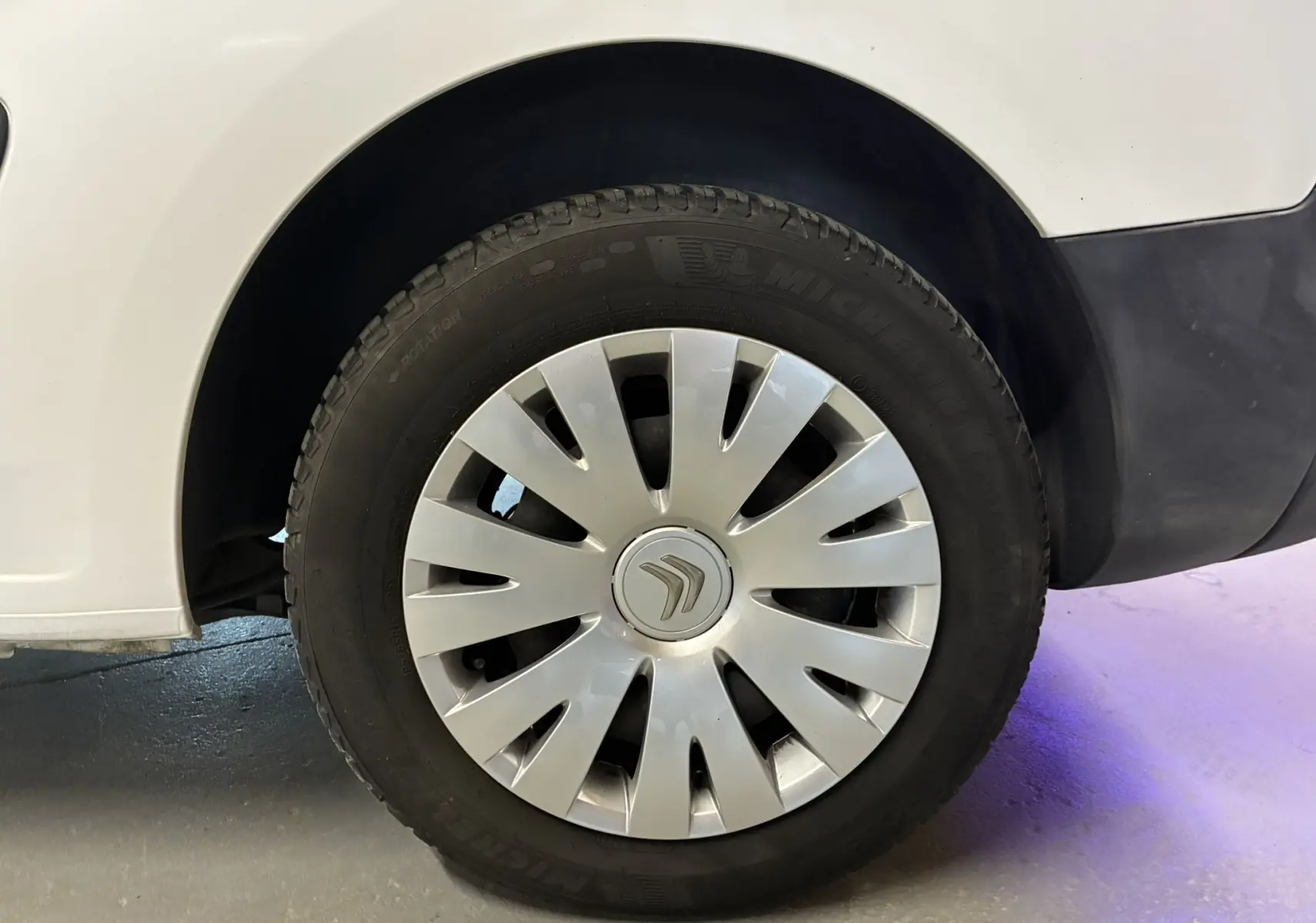 Gros plan sur la roue avant gauche blanche d'un Citroën Berlingo 1.6 BlueHDi 2016 avec enjoliveur argenté et logo Citroën.