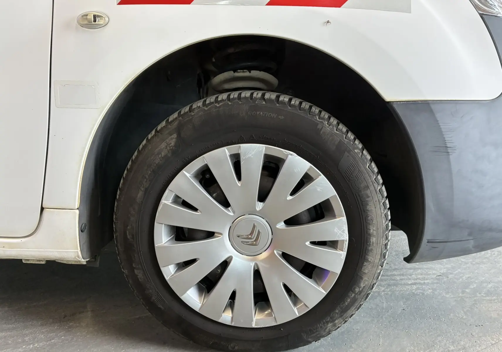 Gros plan sur la roue avant gauche d’un Citroën Berlingo blanc de 2016 avec enjoliveur argenté et pare-chocs noir.