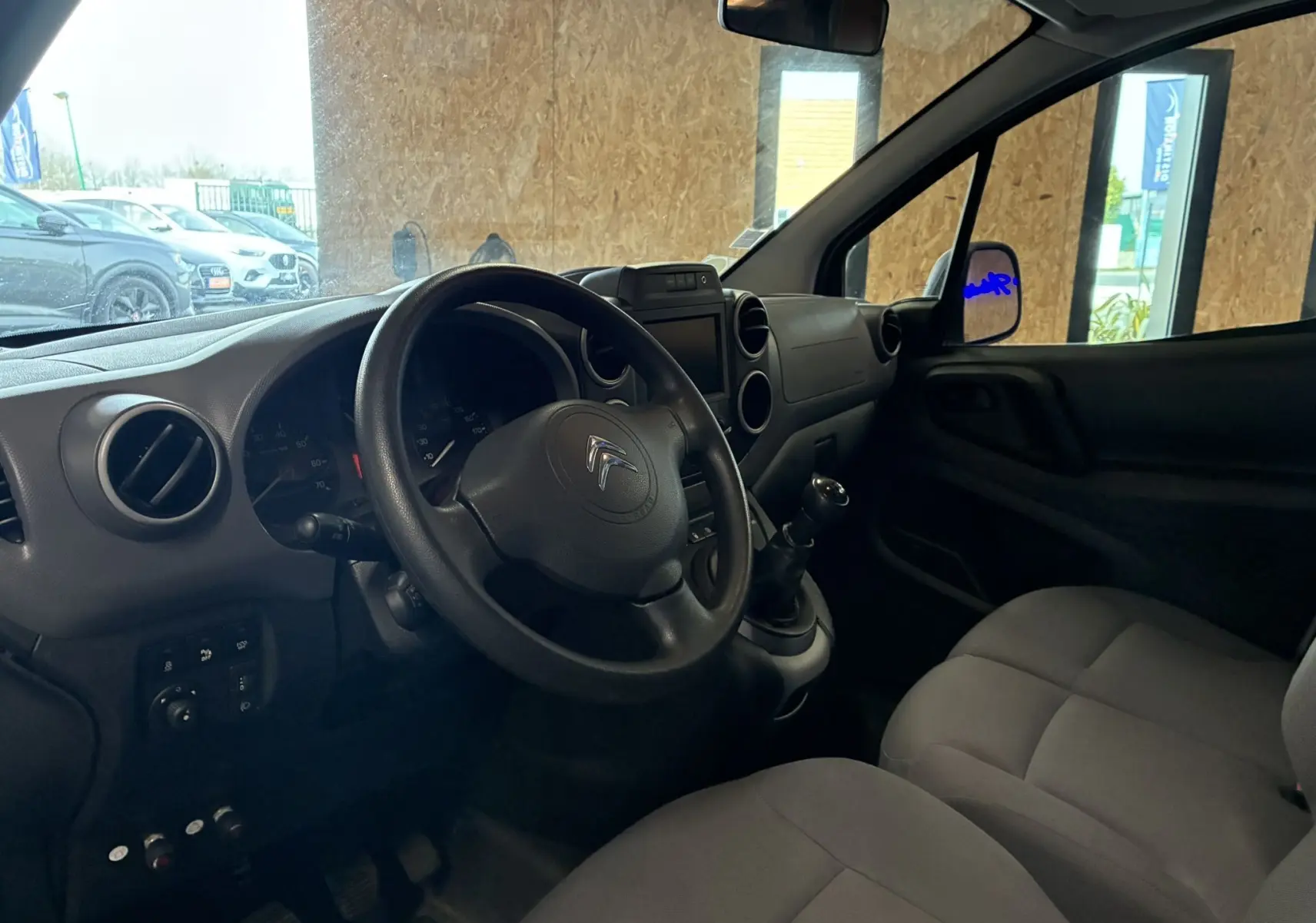 Vue intérieure côté conducteur du Citroën Berlingo blanc 2016, volant, tableau de bord et sièges en tissu gris visibles.