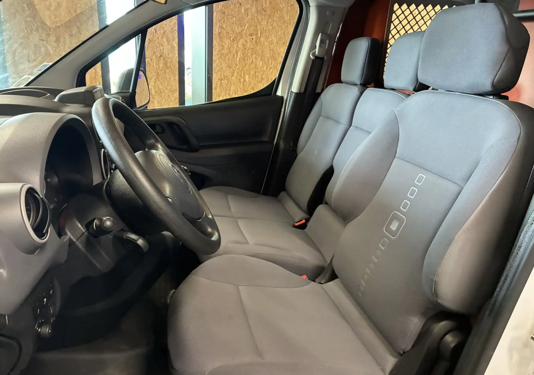Vue intérieure côté conducteur du Citroën Berlingo 1.6 BlueHDi 100 de 2016, sièges tissu gris et tableau de bord noir.