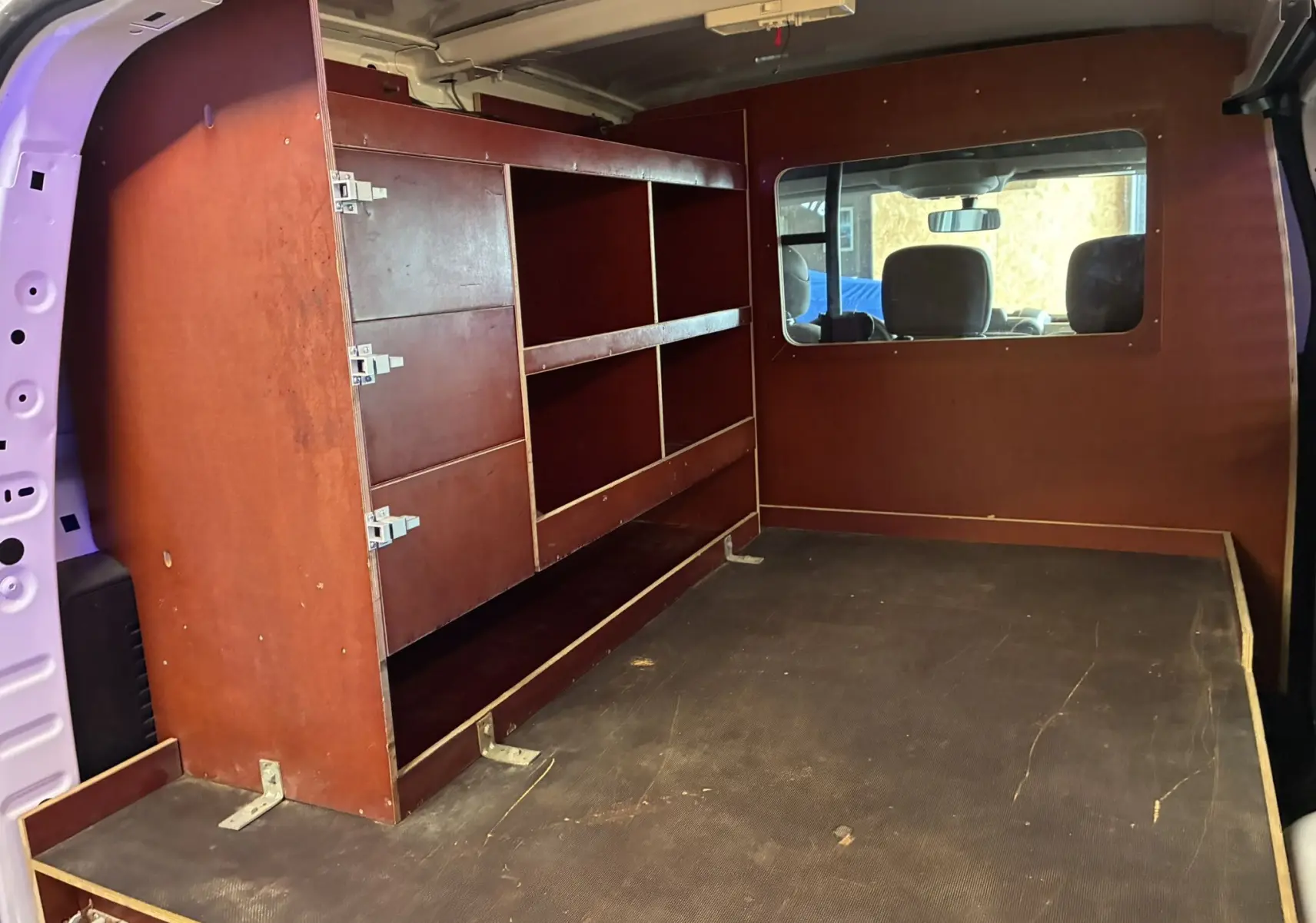 Vue intérieure arrière droite du Citroën Berlingo blanc 2016, montrant un aménagement bois avec étagères et fenêtre vers l'avant.