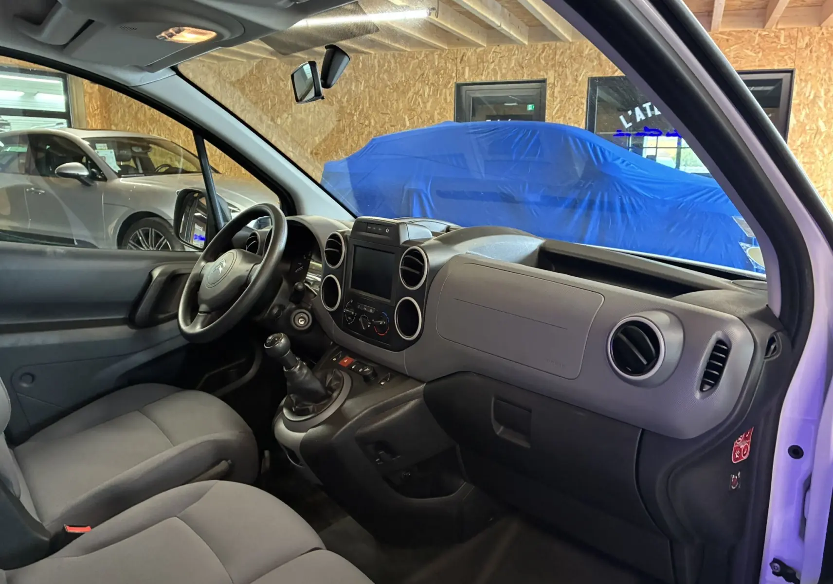 Vue intérieure côté conducteur du Citroën Berlingo blanc 2016, montrant le tableau de bord et la boîte manuelle.