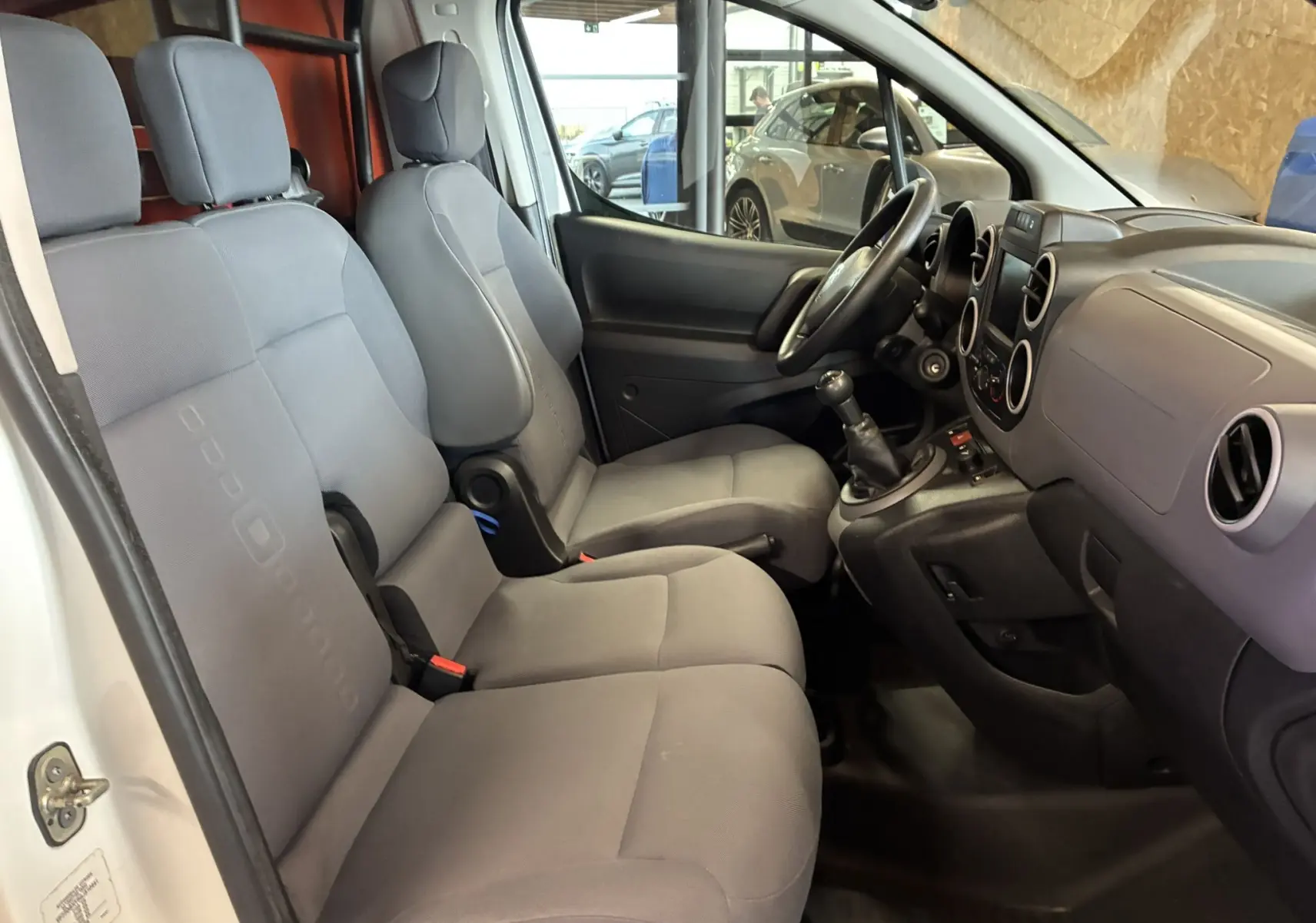 Vue intérieure côté droit du Citroën Berlingo blanc 2016, montrant les sièges avant gris et la console avec boîte manuelle.