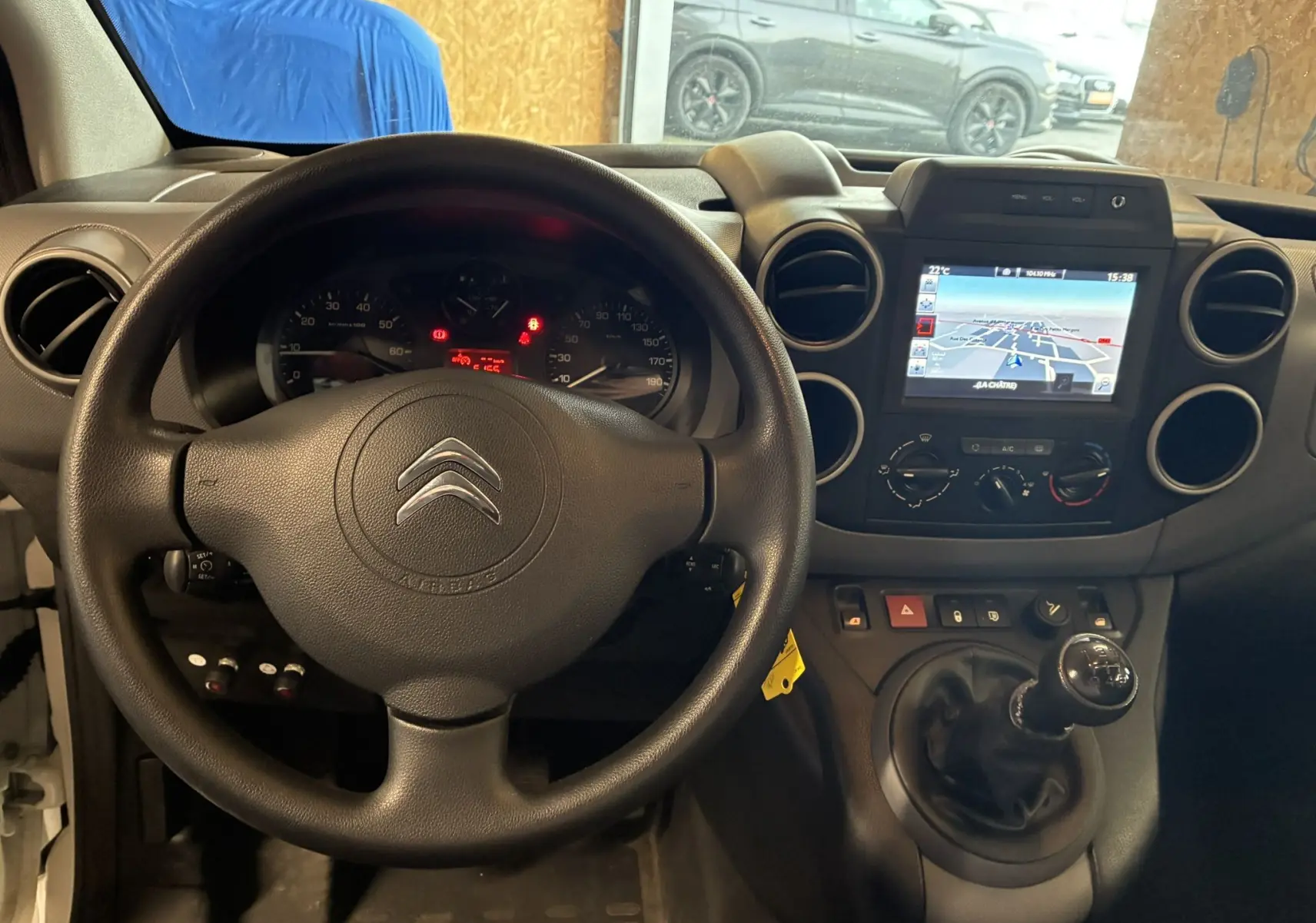 Vue intérieure du tableau de bord du Citroën Berlingo blanc 2016, volant, GPS et levier de vitesse manuel visibles.