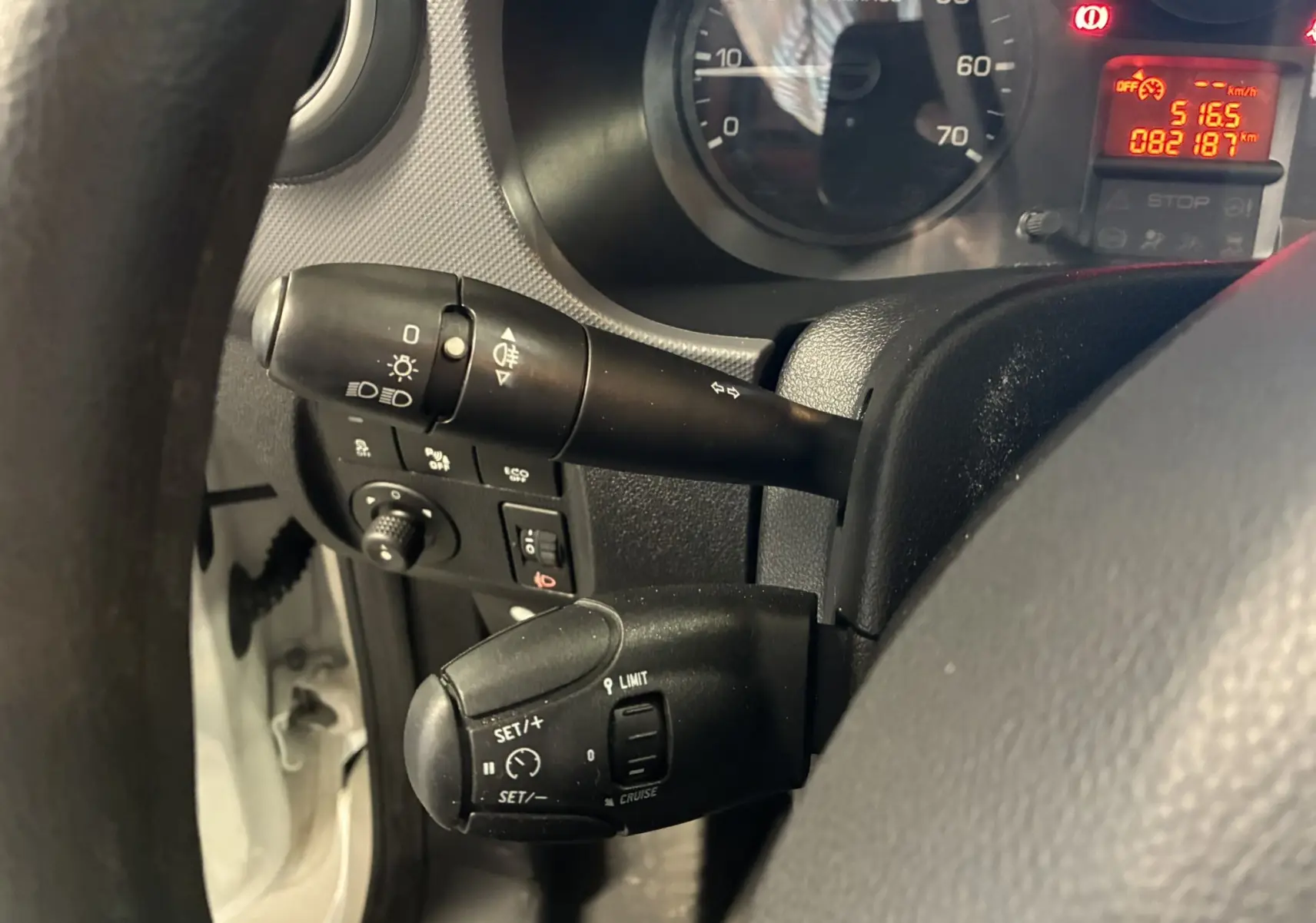 Gros plan sur les commandes au volant noir d’un Citroën Berlingo blanc, tableau de bord et compteur partiellement visibles.