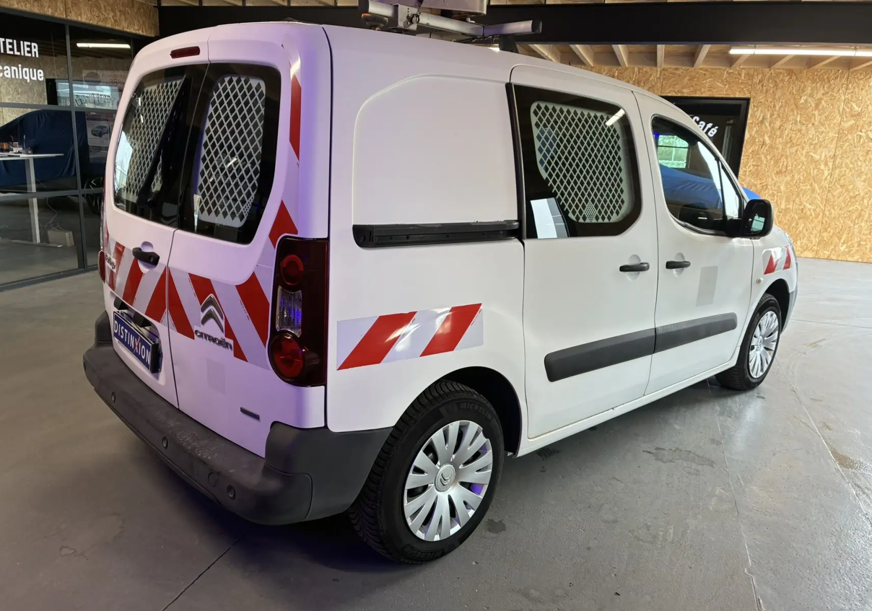 Vue 3/4 arrière droit d'un Citroën Berlingo blanc 2016 avec marquages rouges réfléchissants et grilles de protection aux vitres.