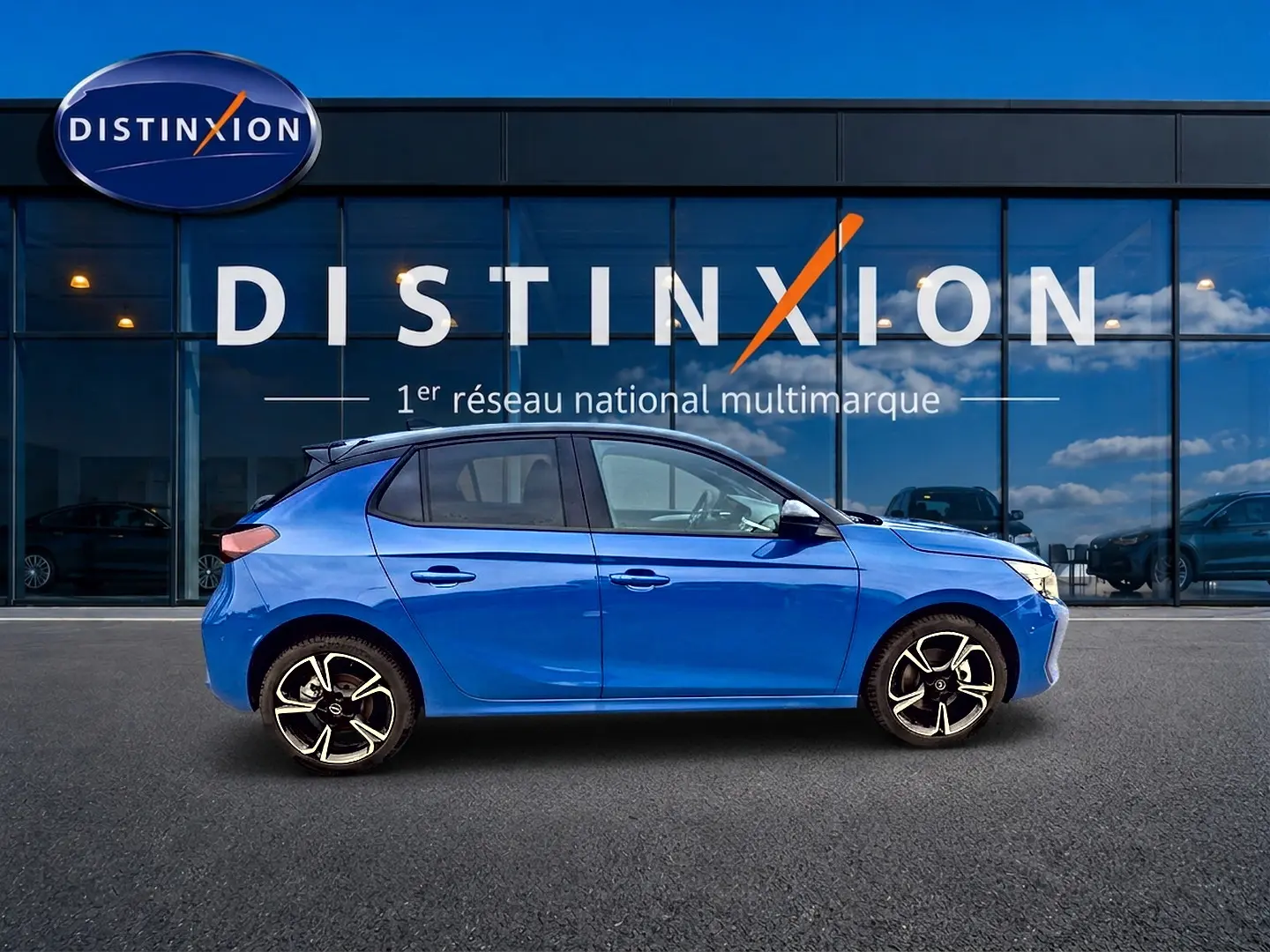Profil côté gauche d'une Opel Corsa 1.2 turbo 100 gs bleu 2025 avec jantes alu et becquet arrière visible devant un showroom Distinxion.
