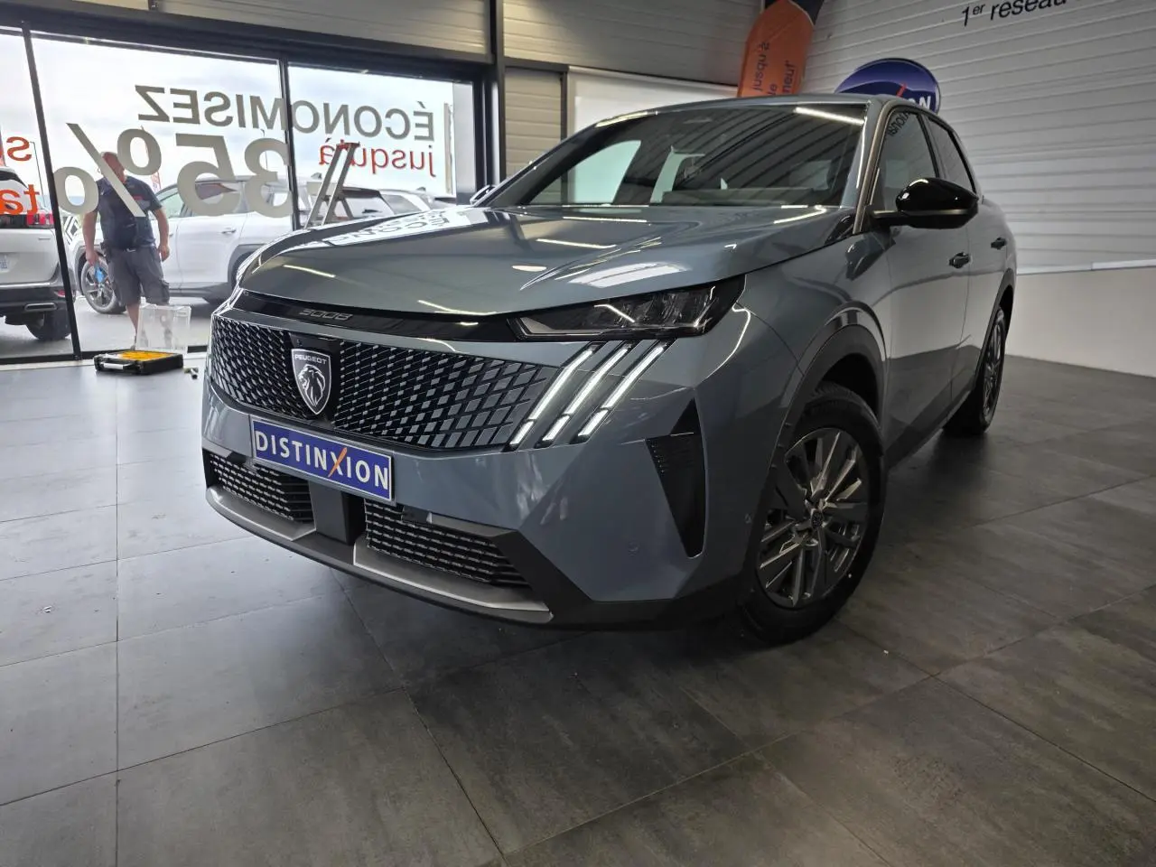 Peugeot 3008 bleu vue 3/4 avant droit en intérieur, avec calandre noire et feux LED à griffes distinctifs.