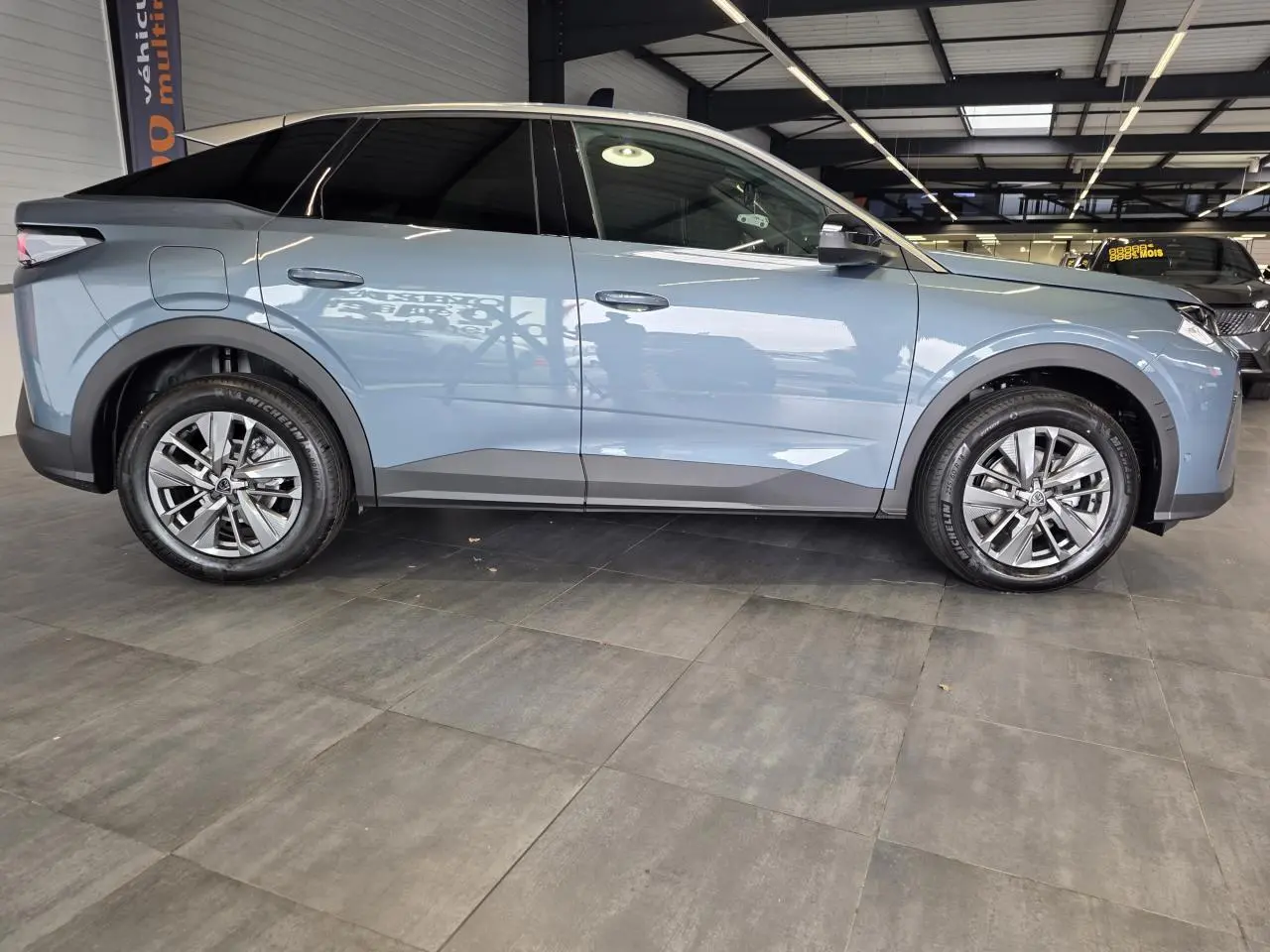 Vue de profil côté gauche d'un Peugeot 3008 hybride bleu avec jantes alliage 18 pouces en intérieur showroom.