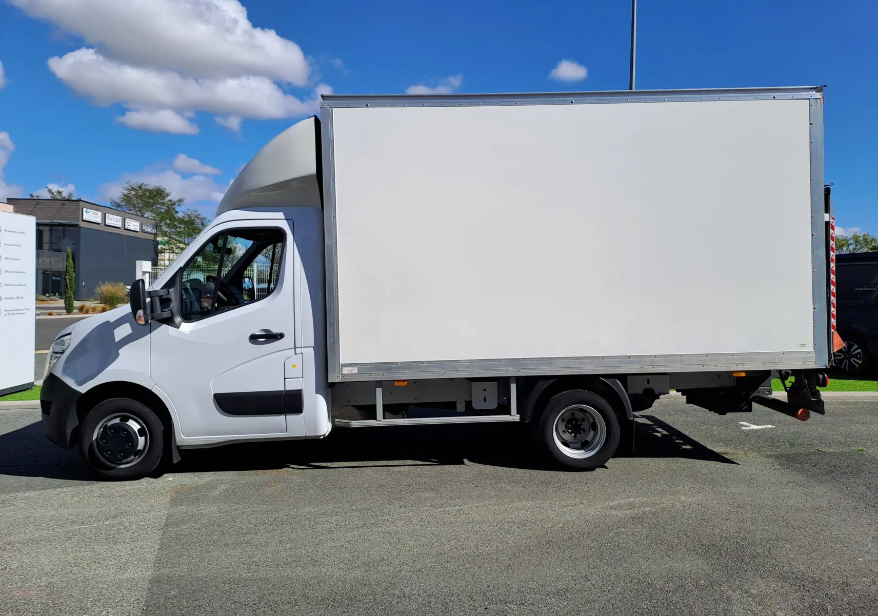 Vue de profil côté gauche d’un Nissan Interstar châssis cabine blanc 2024 avec caisse de livraison sur fond urbain.