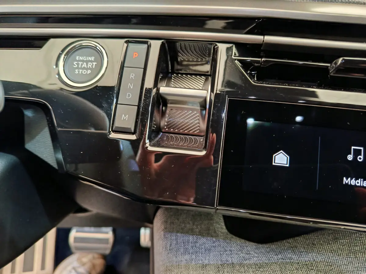 Gros plan sur la console centrale noire brillante du Peugeot 3008 hybride 2025 avec bouton start et commandes de boîte auto.