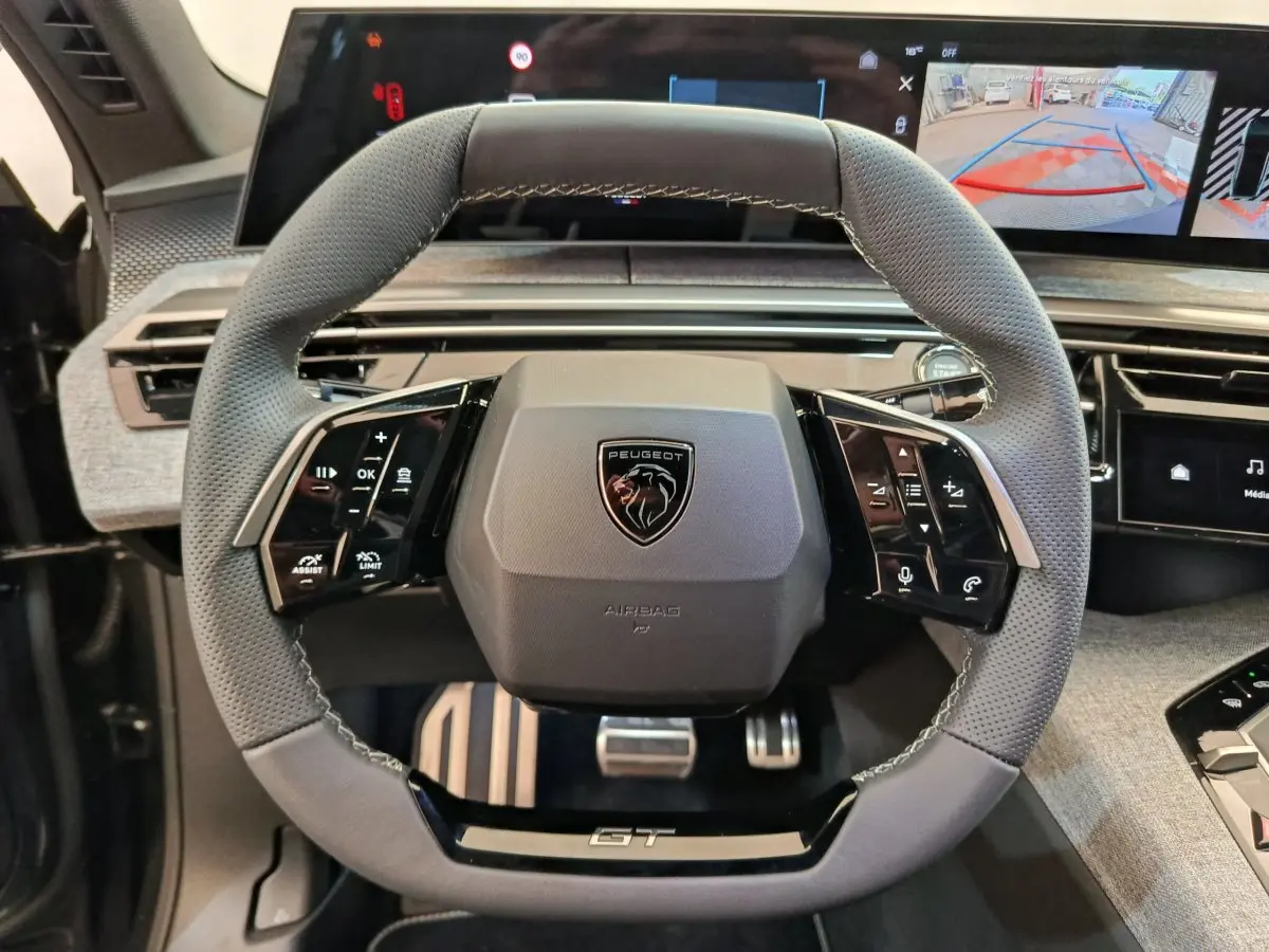 Vue rapprochée du volant cuir gris perforé avec logo Peugeot et badge GT du Peugeot 3008 hybride 2025.