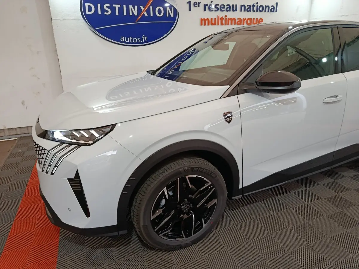 Vue 3/4 avant droit d'un Peugeot 3008 blanc avec jantes noires et calandre distinctive en intérieur showroom