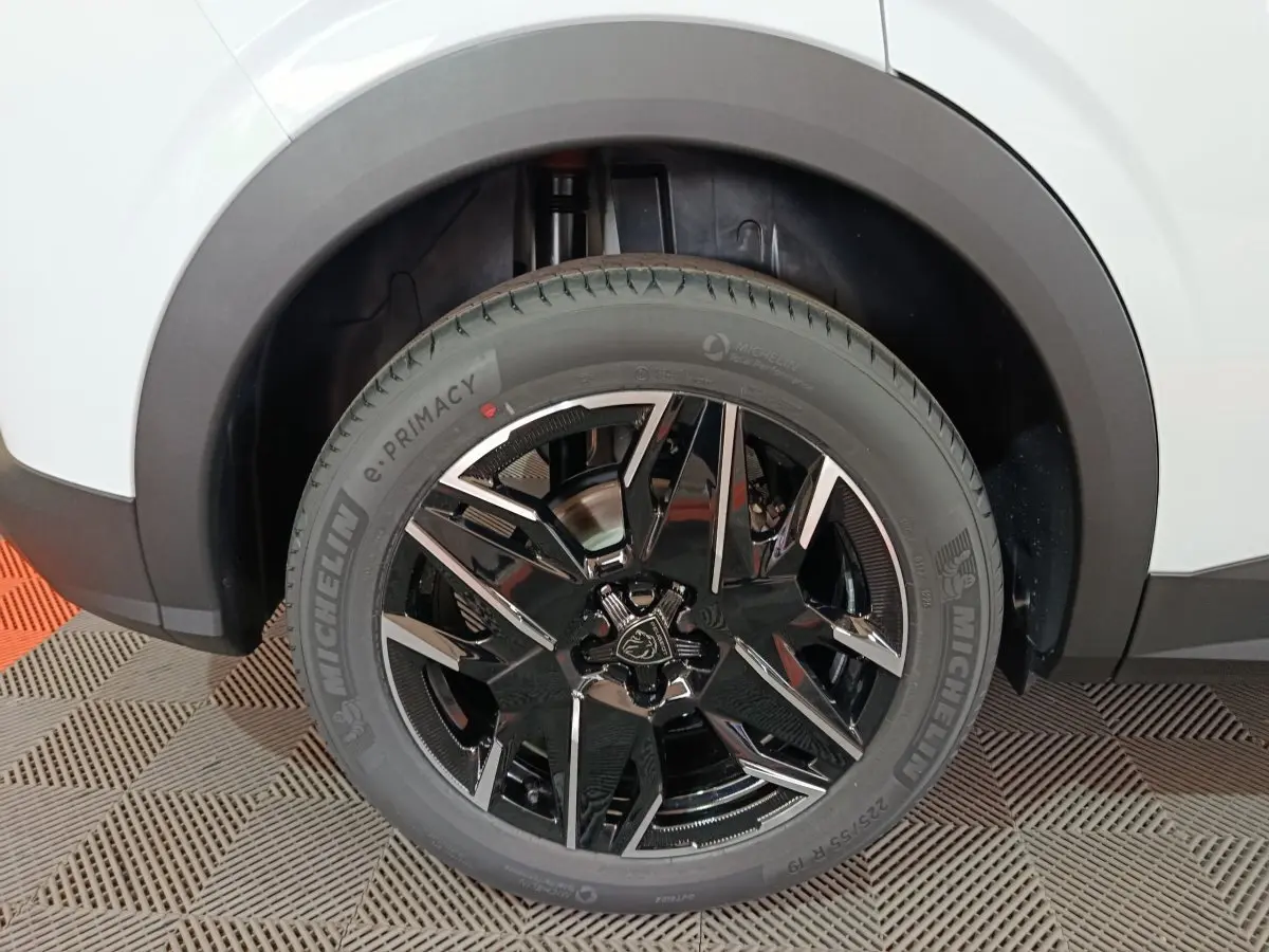 Gros plan sur la roue avant droite du Peugeot 3008 blanc, mettant en valeur la jante noire brillante au design moderne.