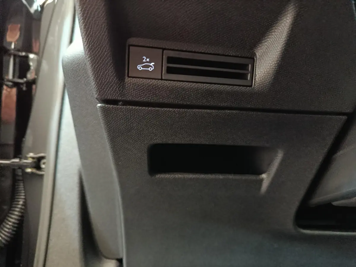 Gros plan sur le bouton d'ouverture électrique du coffre dans l'habitacle noir du Peugeot 3008 hybride blanc 2025.