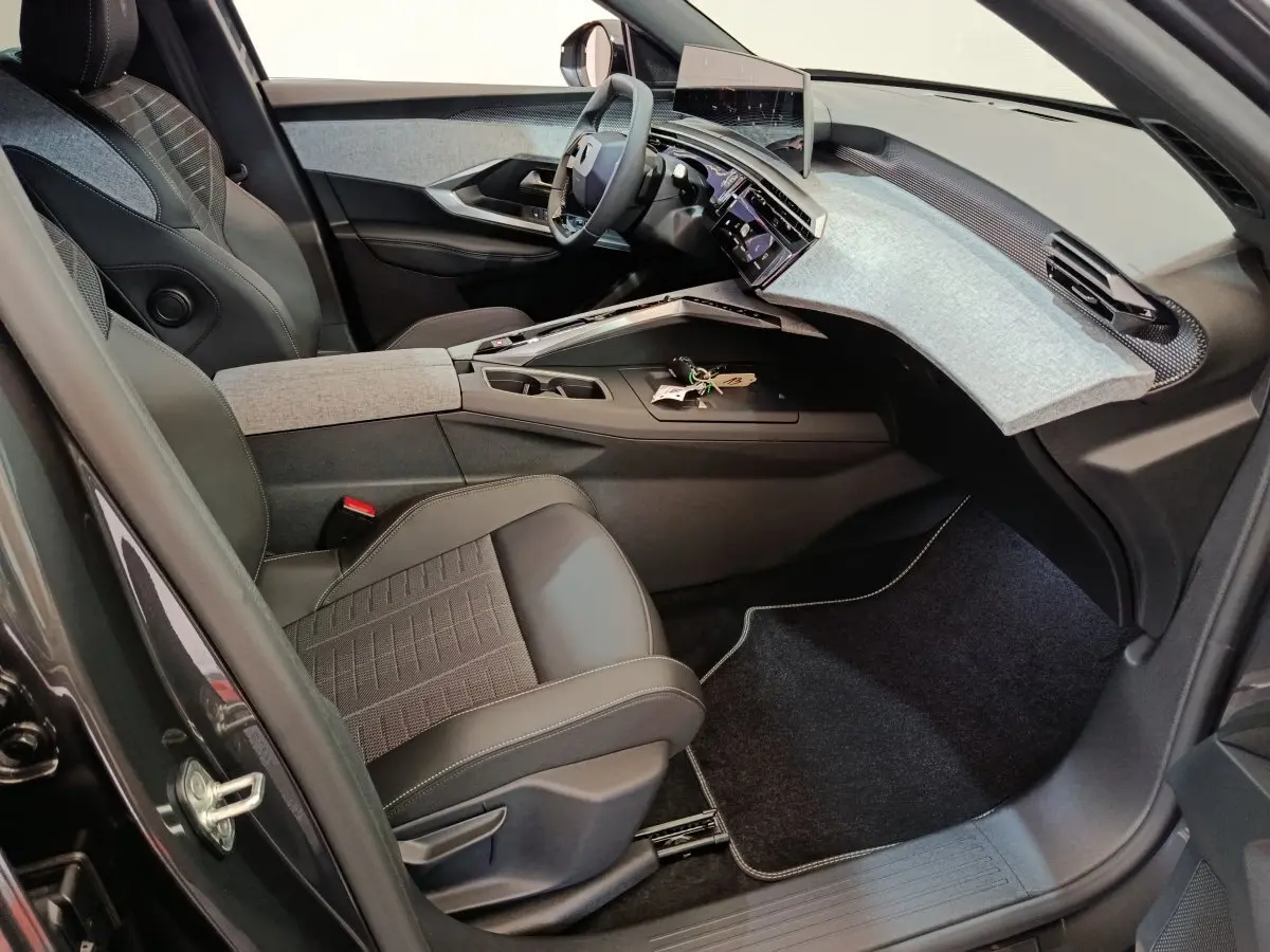 Vue intérieure côté conducteur du Peugeot 3008 1.2 Hybrid 145 GT 2025, tableau de bord moderne avec écran tactile et sièges noirs.