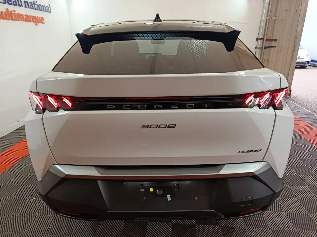 Vue arrière d'un Peugeot 3008 blanc hybride 2025 avec feux LED allumés et logo central noir brillant.