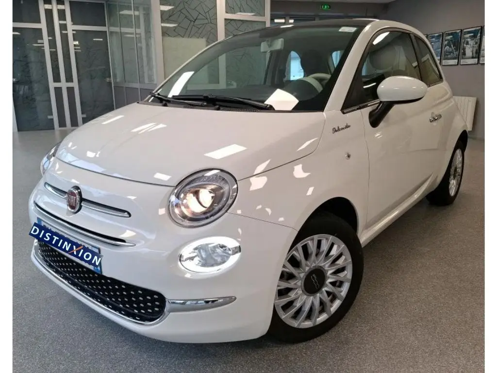 Vue 3/4 avant d'une Fiat 500 blanche Bossa Nova, avec phares allumés et jantes distinctives en concession.