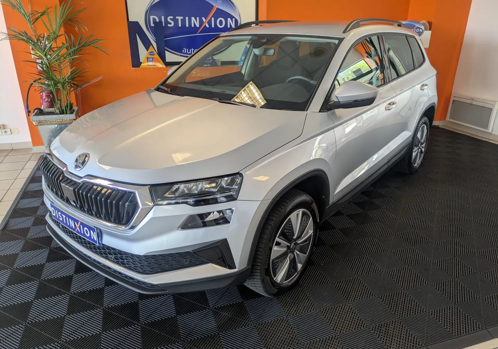 Vue 3/4 avant droite d'un Skoda Karoq gris argent exposé en intérieur avec jantes alliage et calandre chromée.