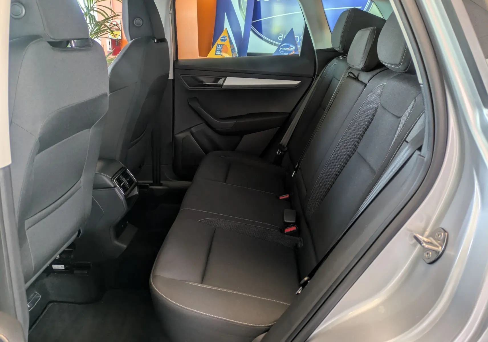 Vue intérieure arrière côté droit du Skoda Karoq gris argent, montrant les sièges noirs et les aérateurs arrière.