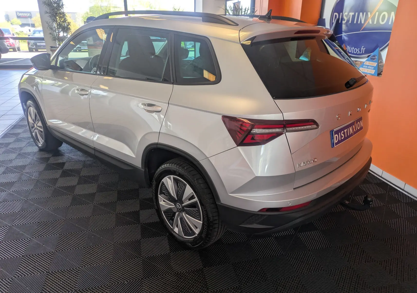 Vue 3/4 arrière droite d'un Skoda Karoq gris argent 2023 avec jantes alliage et hayon électrique en intérieur showroom.