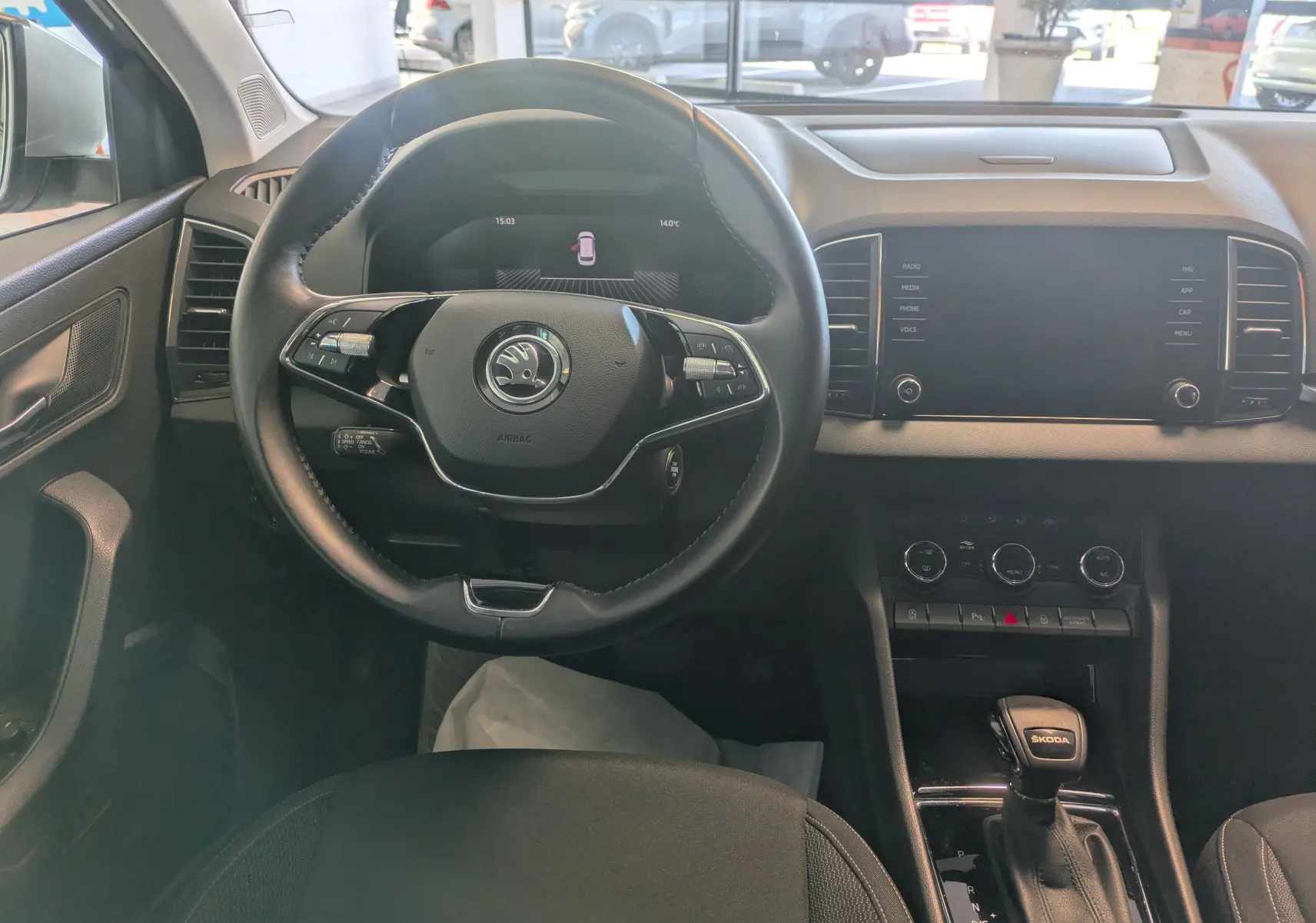 Vue intérieure centrée sur le volant noir et le tableau de bord avec écran tactile du Skoda Karoq gris argent 2023.