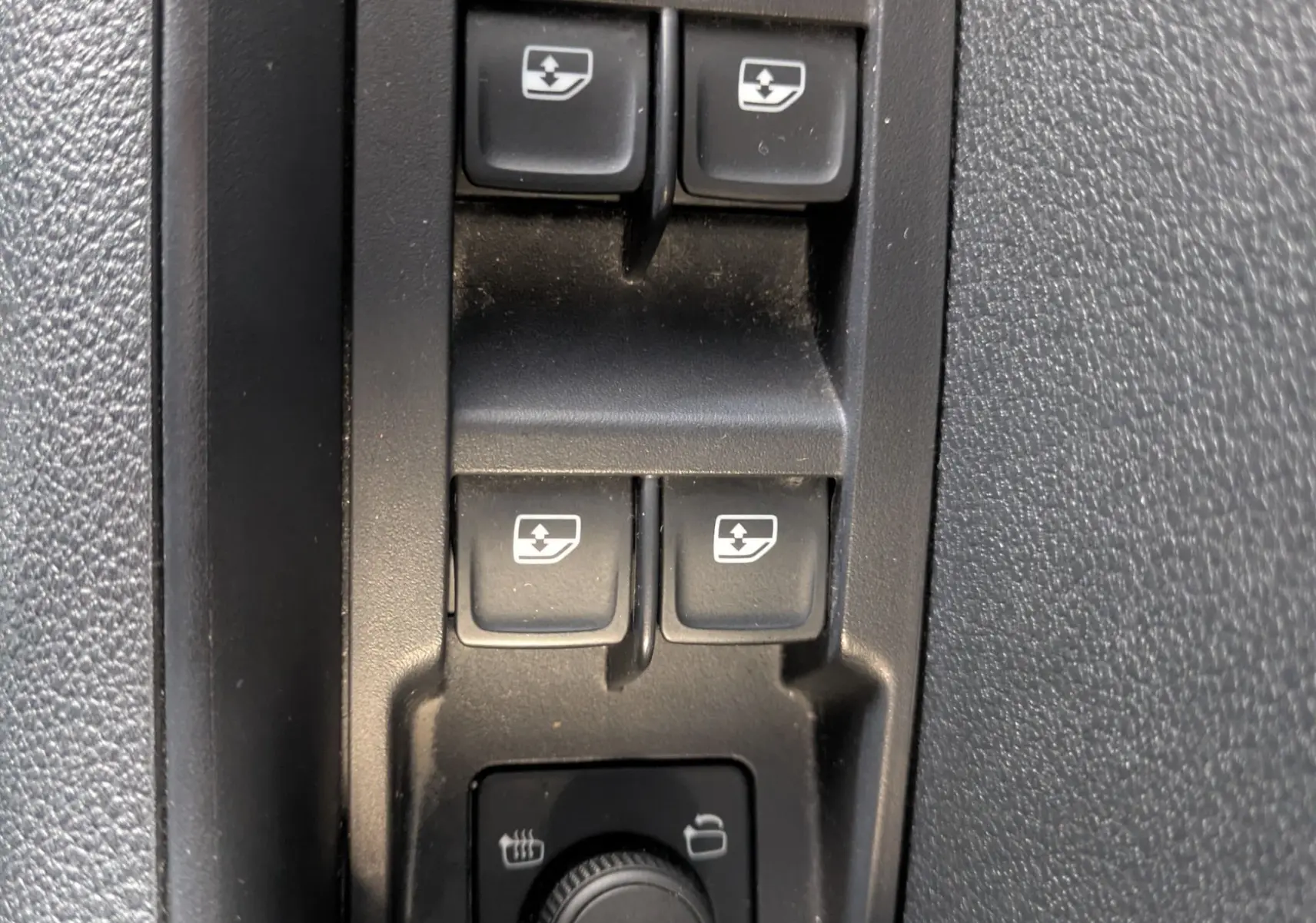 Gros plan sur les commandes des vitres électriques et réglage des rétroviseurs dans l'habitacle noir du Skoda Karoq 2023.