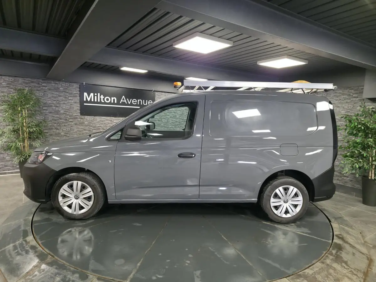 Vue latérale droite d’un Volkswagen Caddy Cargo gris 2022 avec galerie de toit et jantes acier noires.