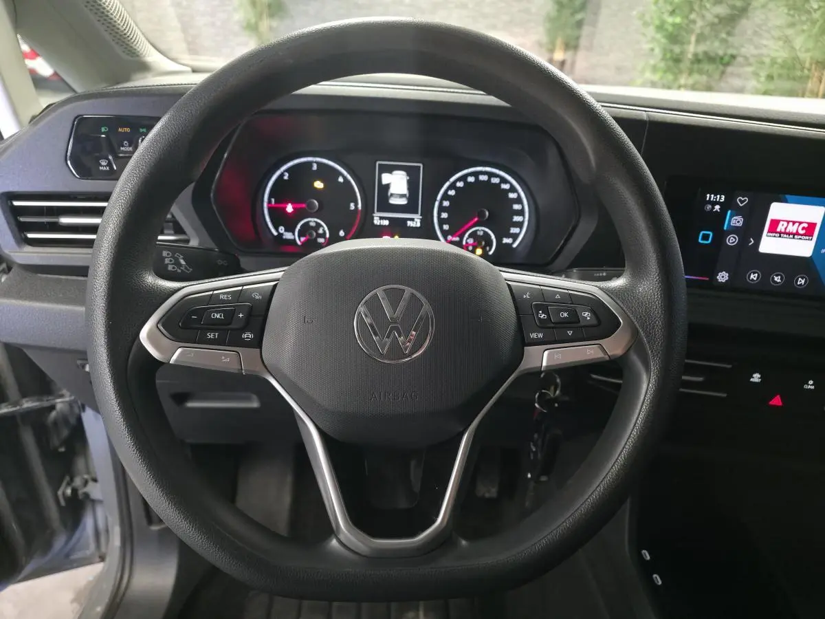 Vue intérieure centrée sur le volant noir du Volkswagen Caddy Cargo 2022 avec tableau de bord et écran tactile.