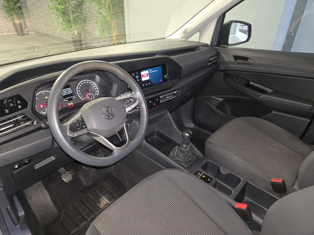 Vue intérieure côté conducteur du Volkswagen Caddy Cargo 2022, tableau de bord noir et sièges tissu gris foncé.