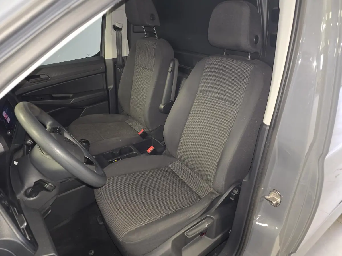 Vue intérieure côté conducteur du Volkswagen Caddy Cargo gris 2022, montrant les sièges avant en tissu et la cloison de séparation.
