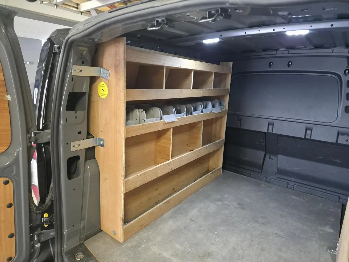 Vue intérieure arrière du Volkswagen Caddy Cargo gris 2022, montrant l'aménagement bois avec étagères et éclairage LED.