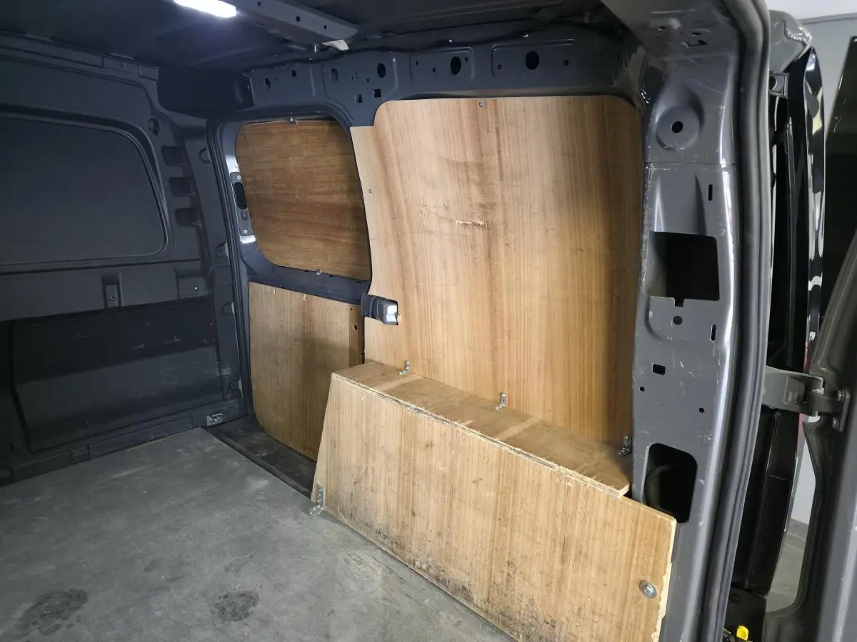 Vue intérieure côté droit du fourgon Volkswagen Caddy Cargo gris 2022 avec cloison bois et plancher caoutchouc.