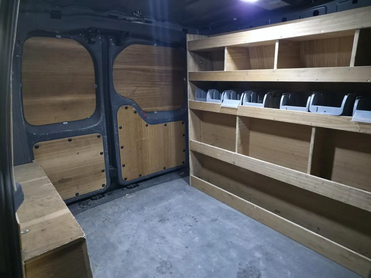Vue intérieure arrière du fourgon Volkswagen Caddy Cargo gris, montrant les aménagements en bois pour rangement.
