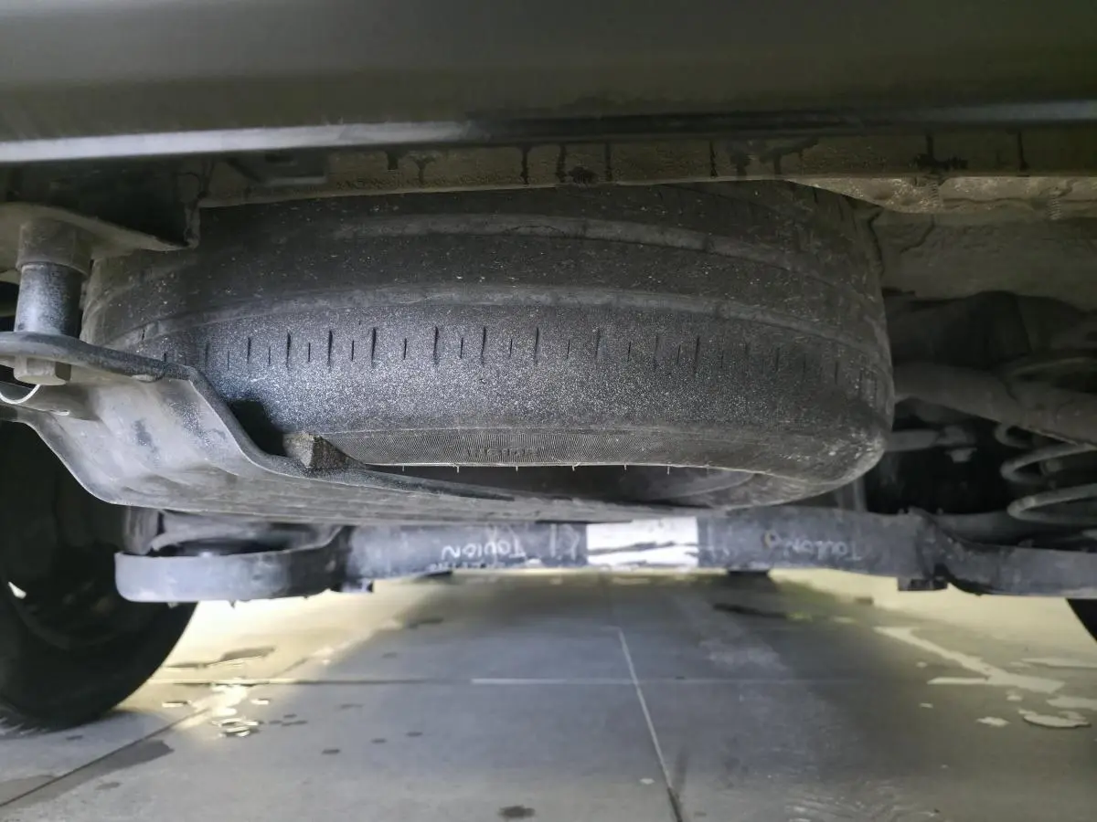 Vue en contre-plongée sous un Volkswagen Caddy Cargo gris montrant la roue de secours et le train arrière.