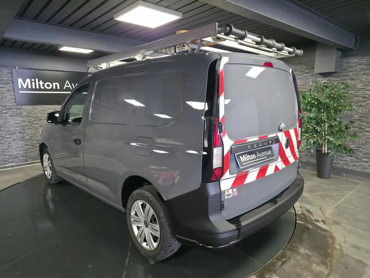 Vue 3/4 arrière droite d’un Volkswagen Caddy Cargo gris avec marquage rouge et blanc sur les portes arrière et galerie de toit.