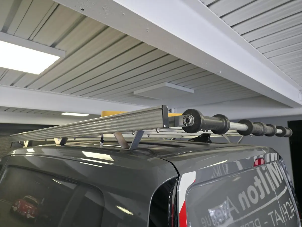 Vue arrière en 3/4 droit d’un Volkswagen Caddy Cargo gris avec galerie de toit et échelle fixée dessus dans un garage.