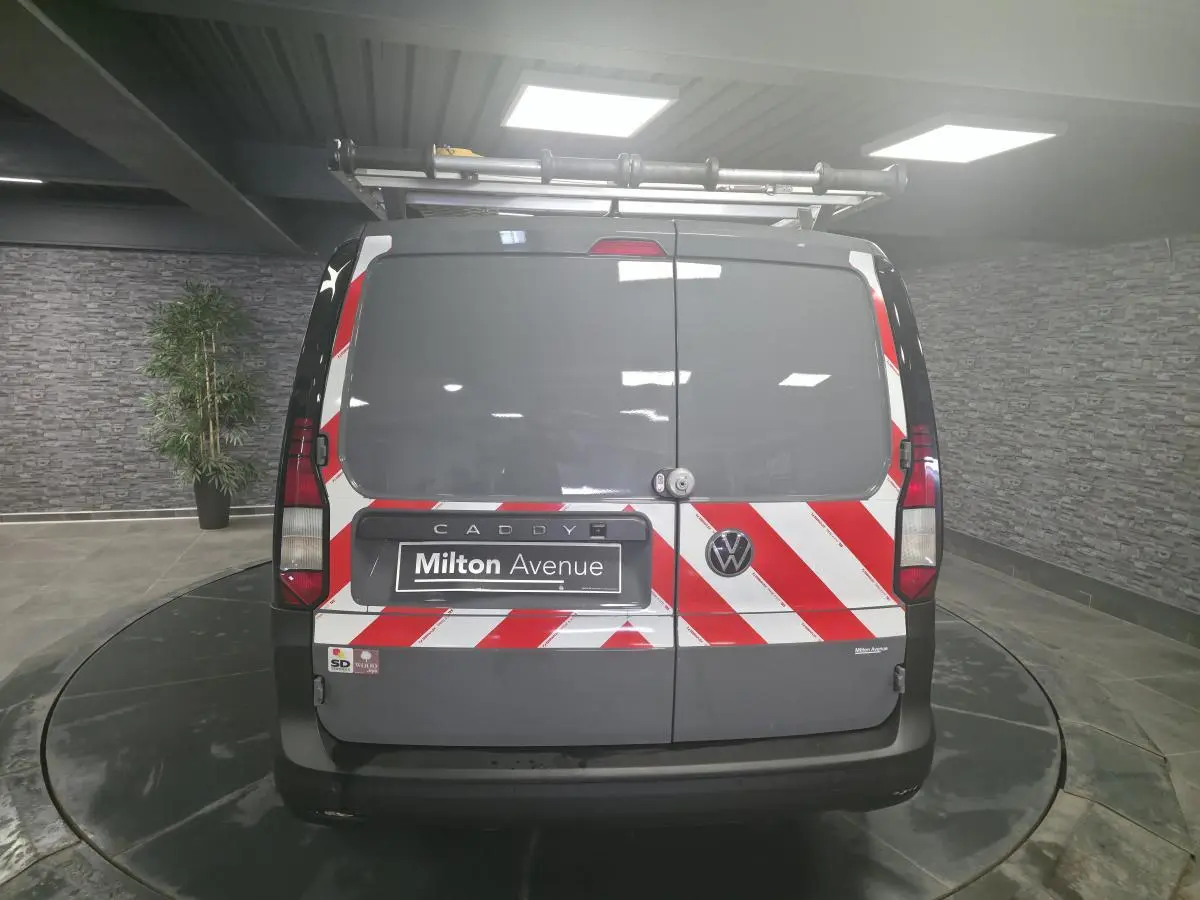 Vue arrière d’un Volkswagen Caddy Cargo gris 2022 avec bandes réfléchissantes rouges et blanches et galerie de toit.