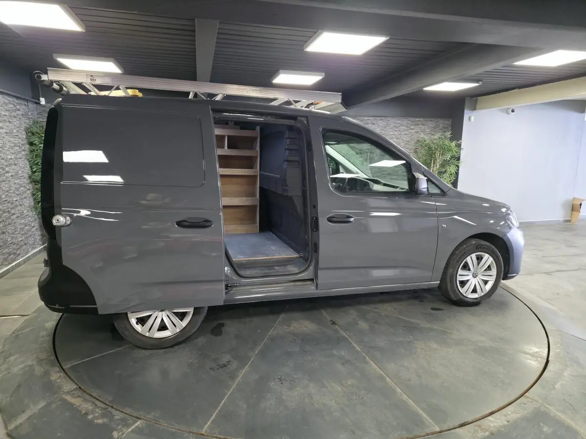 Vue latérale droite d'un Volkswagen Caddy Cargo gris 2022 avec porte coulissante ouverte révélant un aménagement bois intérieur.