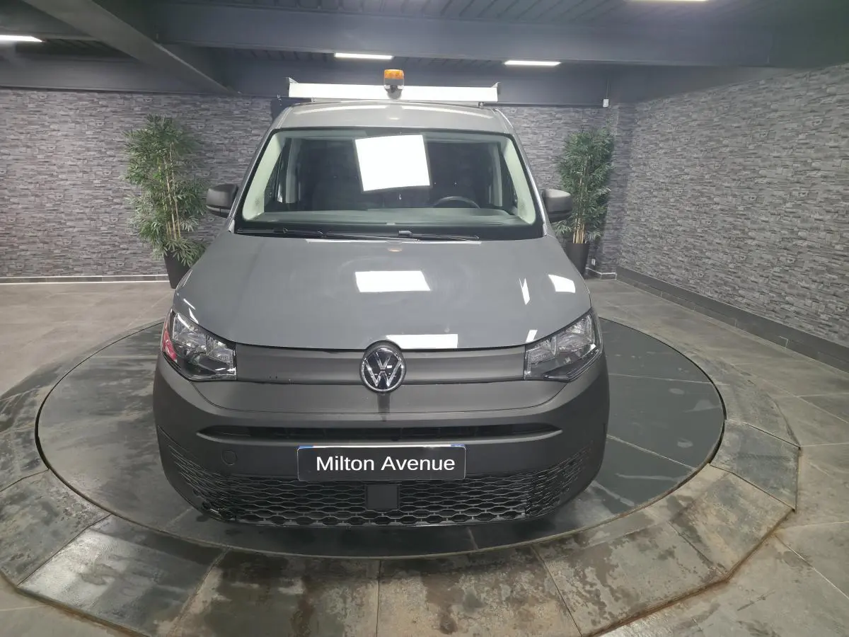 Vue frontale d'un Volkswagen Caddy Cargo gris 2022 avec galerie de toit et feux halogènes allumés en intérieur.