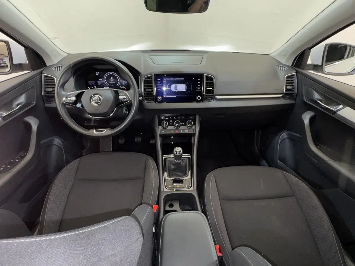 Vue intérieure avant du Skoda Karoq 2024, tableau de bord noir avec écran tactile central et volant cuir multifonctions.