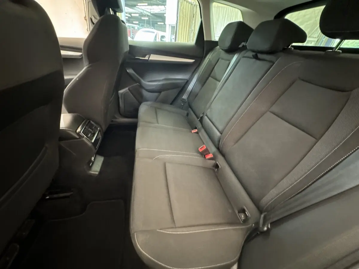 Vue intérieure côté droit des sièges arrière noirs du Skoda Karoq 2024 avec accoudoir central et ceintures visibles.