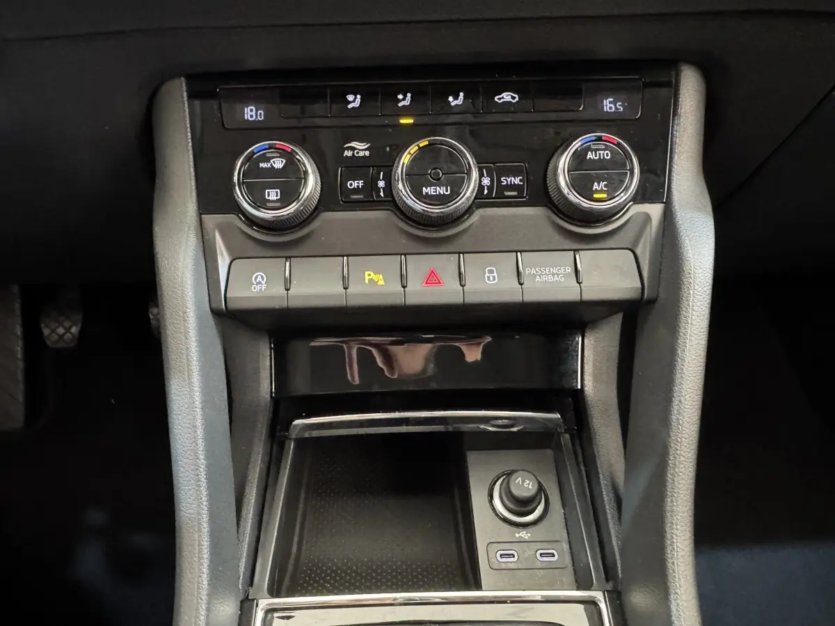 Vue rapprochée du tableau de bord central noir du Skoda Karoq 2024 avec commandes climatisation et prises USB visibles.