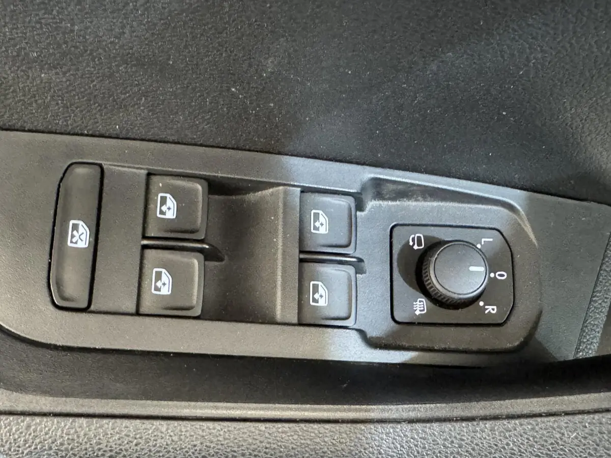 Gros plan sur les commandes de lève-vitres et réglage des rétroviseurs côté conducteur d’un Skoda Karoq blanc 2024.