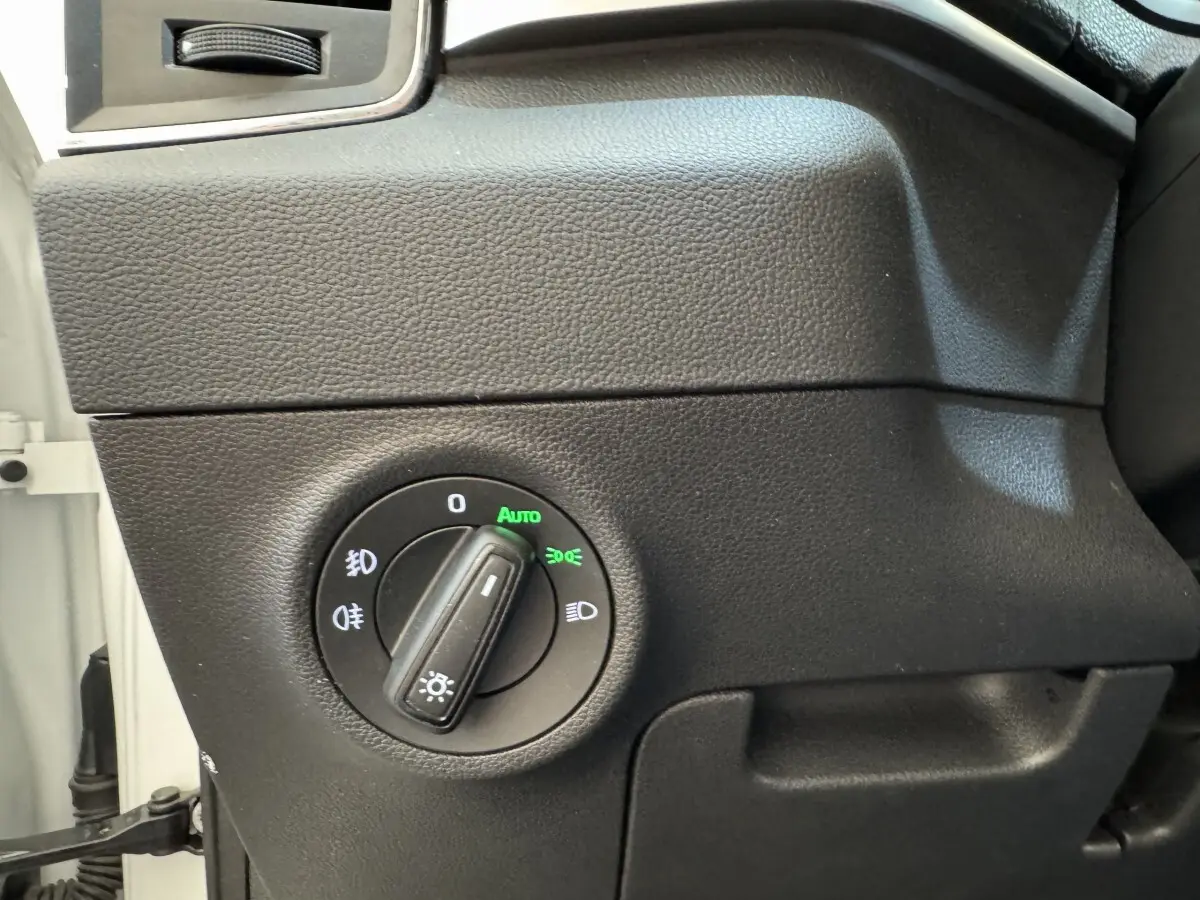 Gros plan sur le bouton de commande des phares avec réglage automatique dans l'habitacle noir d'une Skoda Karoq blanc.