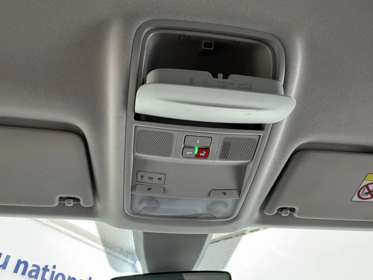 Vue intérieure du plafond avant du Skoda Karoq blanc 2024, montrant les commandes d'éclairage et le rangement lunettes ouvert.