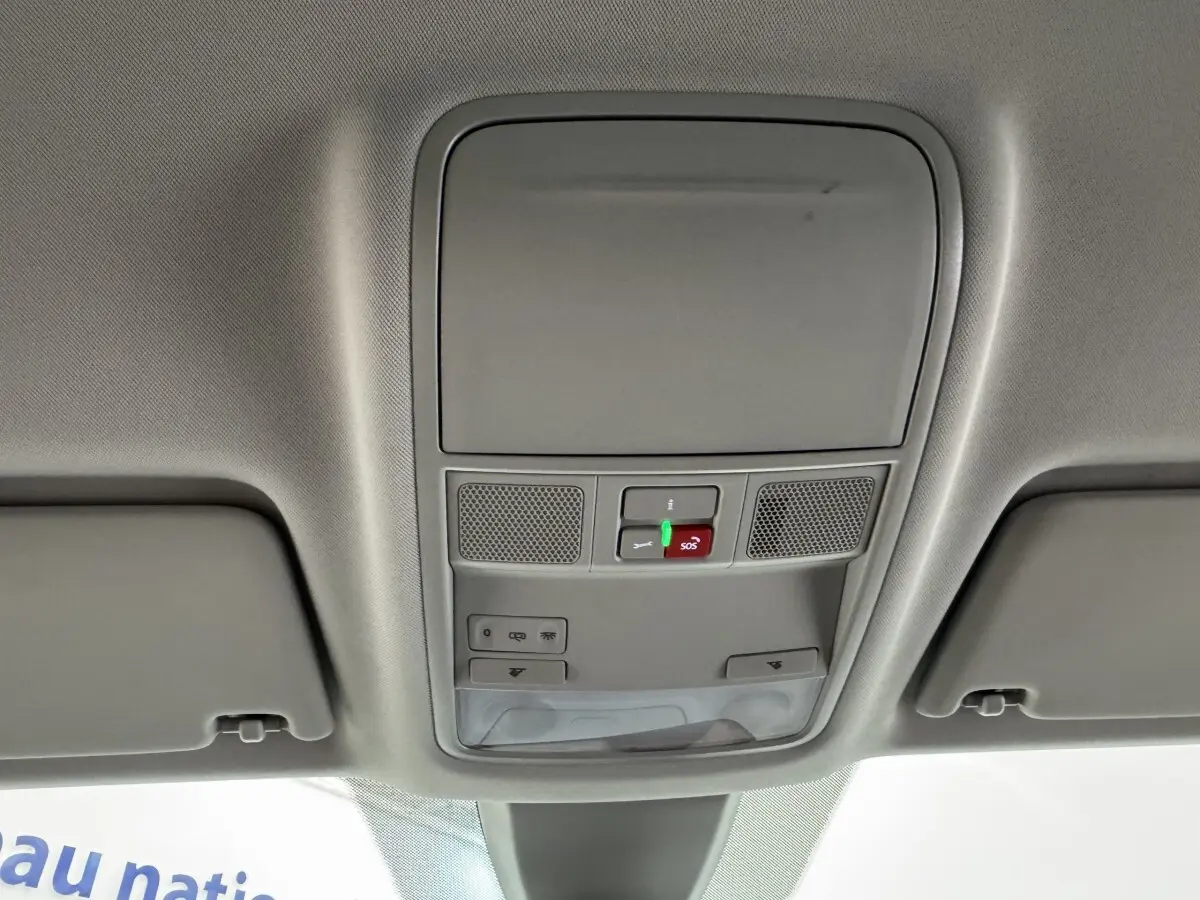 Vue intérieure du plafond avant gris clair du Skoda Karoq blanc 2024 avec commandes d'éclairage et bouton SOS éclairé.
