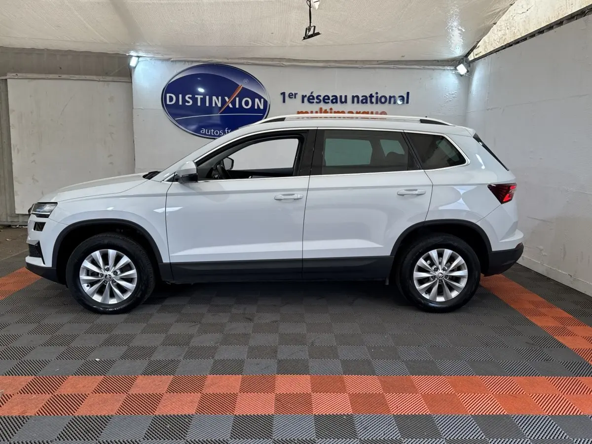 Vue latérale droite d'un Skoda Karoq blanc 2024, SUV compact avec jantes alliage et barres de toit noires.