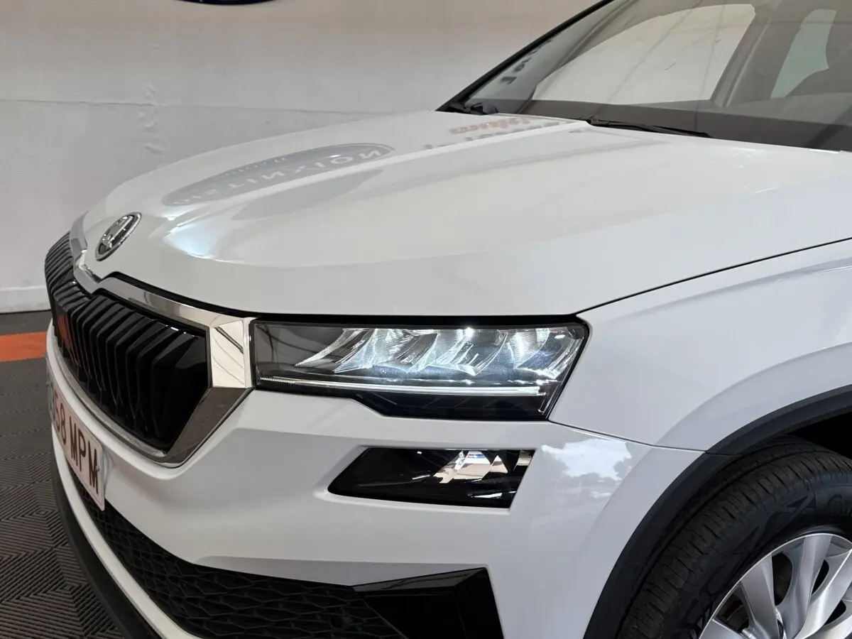 Vue 3/4 avant droit d'un Skoda Karoq blanc 2024 avec calandre noire et phares LED distinctifs.