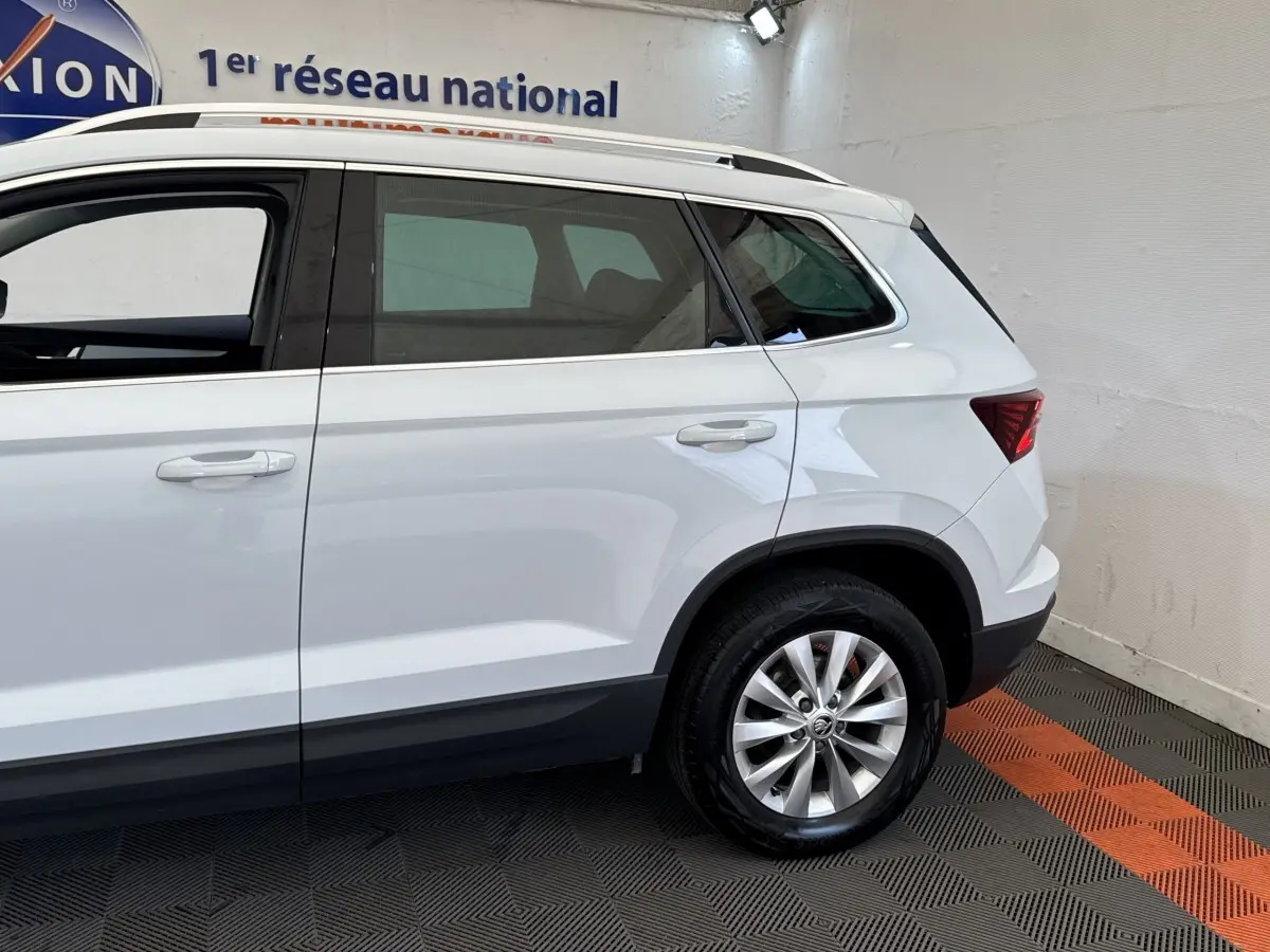 Vue latérale côté droit du SUV blanc SKODA KAROQ 2024 avec jantes alliage et rails de toit noirs visibles.